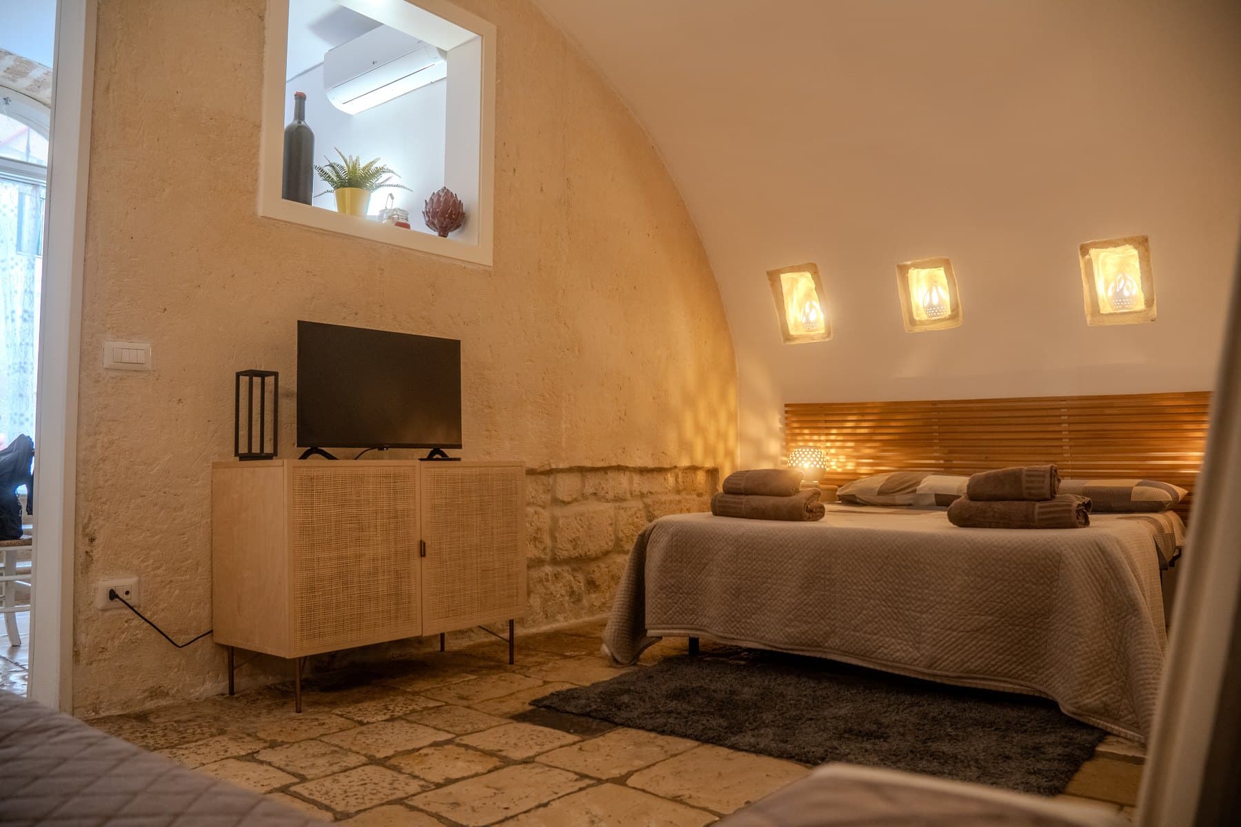 La camera vista d’insieme, con il muro in pietra viva, la credenza e il televisore