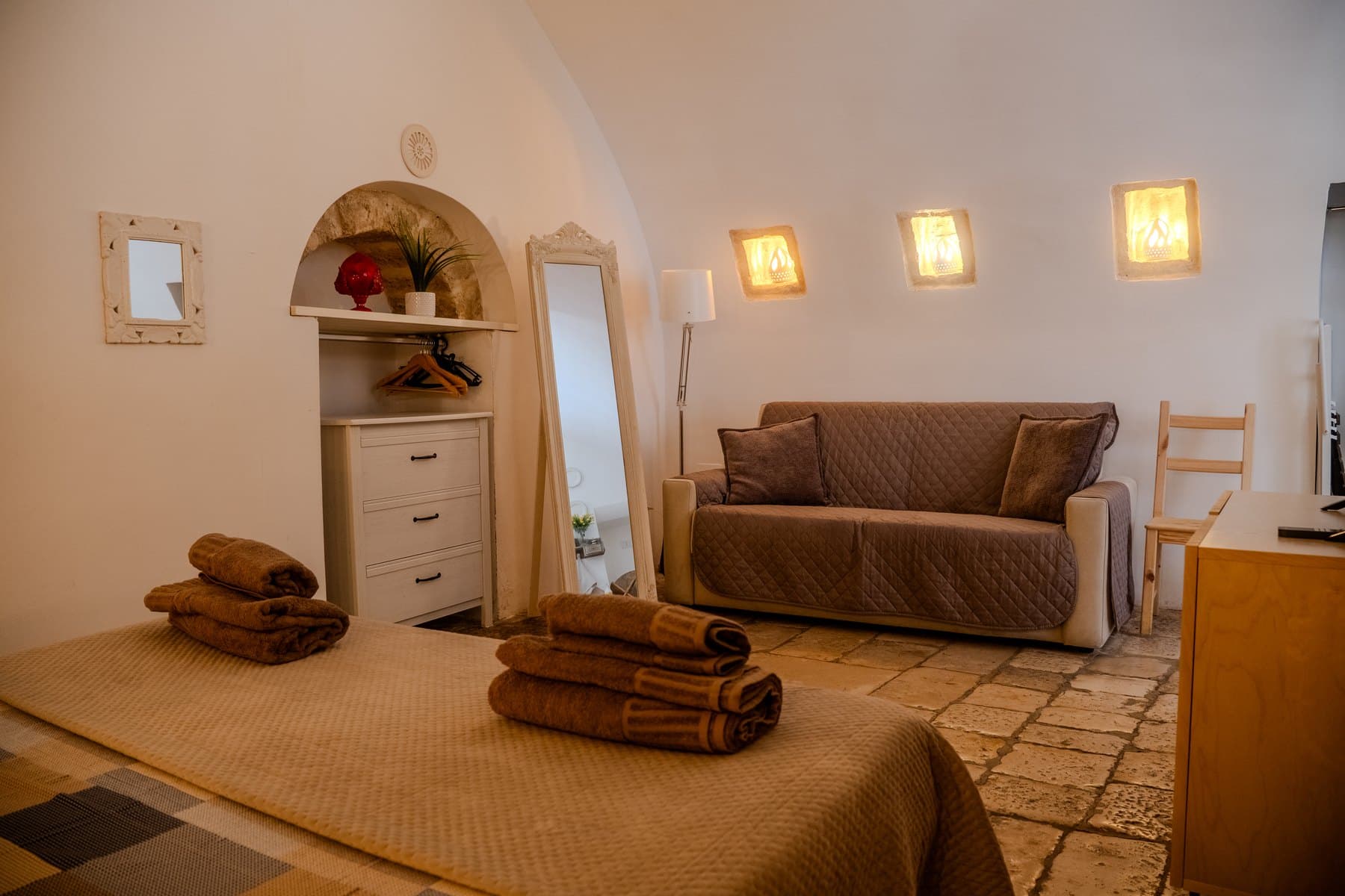 The living area under the barrel vault, with the sofa bed, floor mirror, three lit niches and the original stone floor